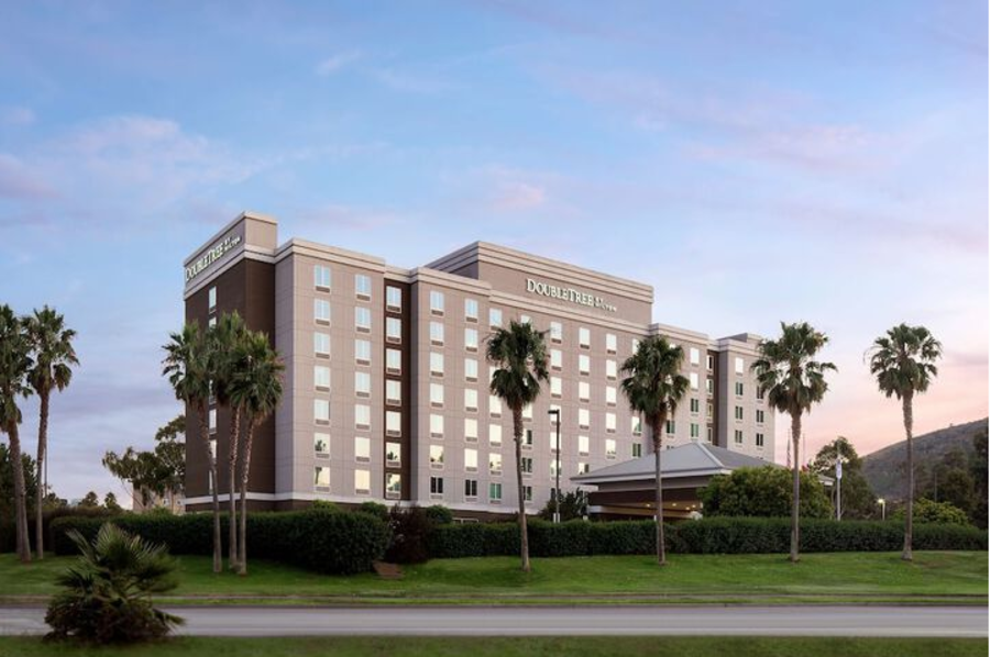 A tall hotel building with a sign on top surrounded by palm trees and grass.